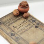 An antique cookbook lying open on a table beside a handful of walnuts