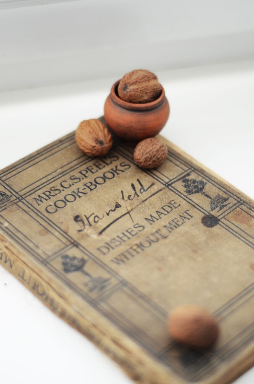 An antique cookbook lying open on a table beside a handful of walnuts